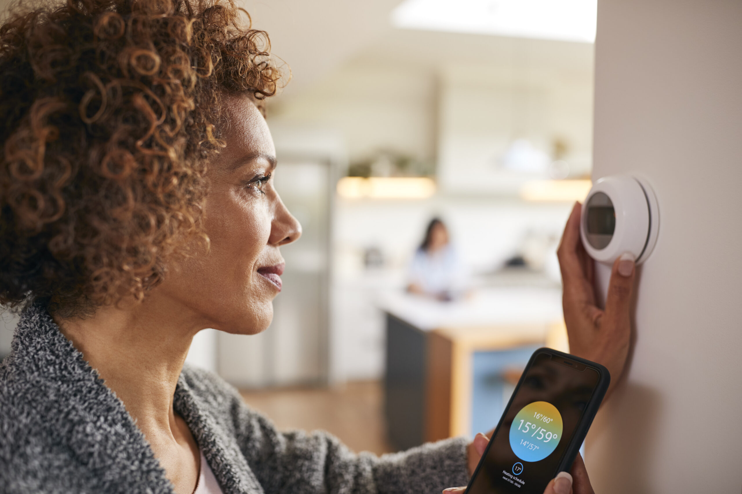 Mature Woman Using App On Phone To Control Digital Central Heating Thermostat At Home smart climate